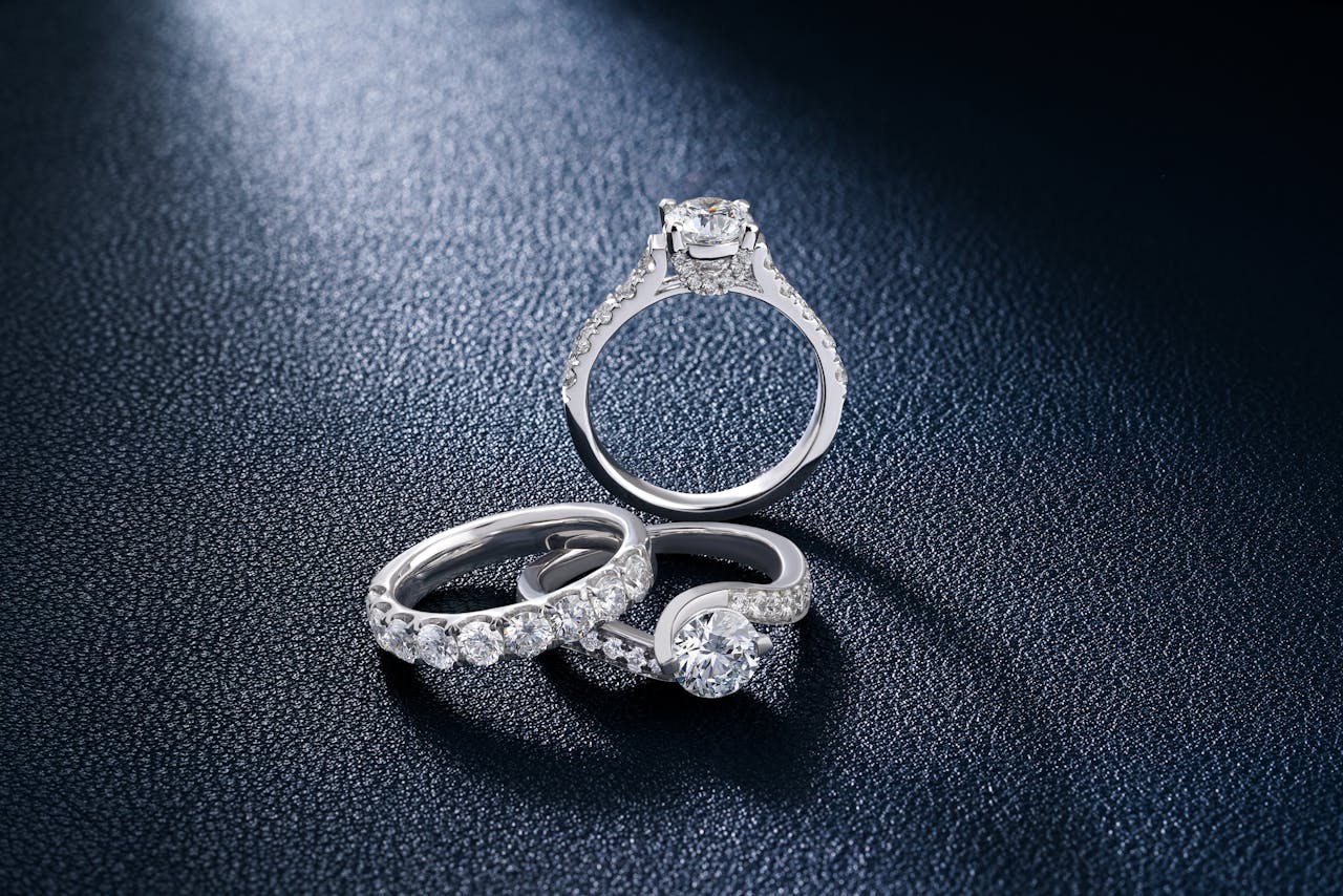 gallery-3 Close-up of luxurious diamond engagement and wedding rings on a textured surface, showcasing elegance and craftsmanship.