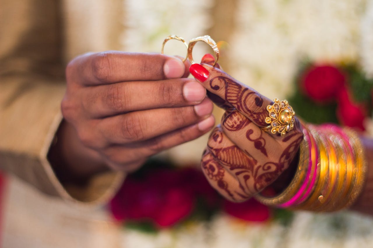 gallery-4 Close-up of hands with henna and jewelry during a traditional Indian wedding ceremony, exchanging rings.