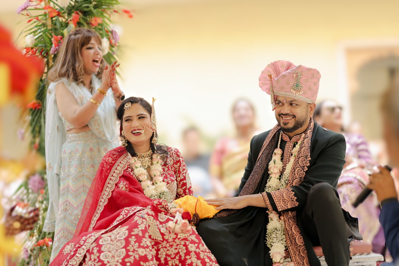 hero-img-01 Happy Indian couple in traditional attire at a festive wedding ceremony, surrounded by joyous guests.